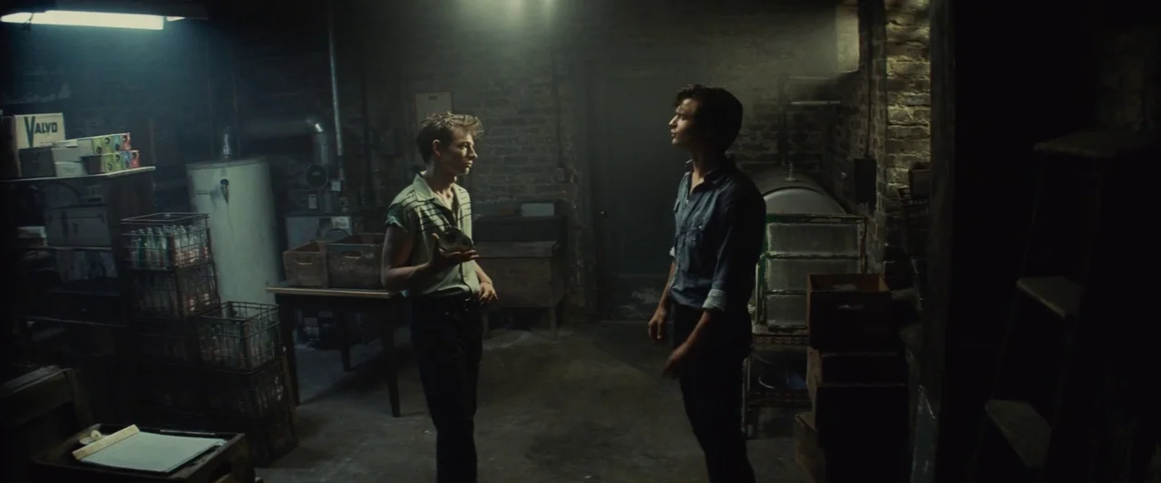 Making of: West Side Story (2021) movie still: medium — A dimly lit basement features bare brick walls and stacks of wooden storage crates. Two…