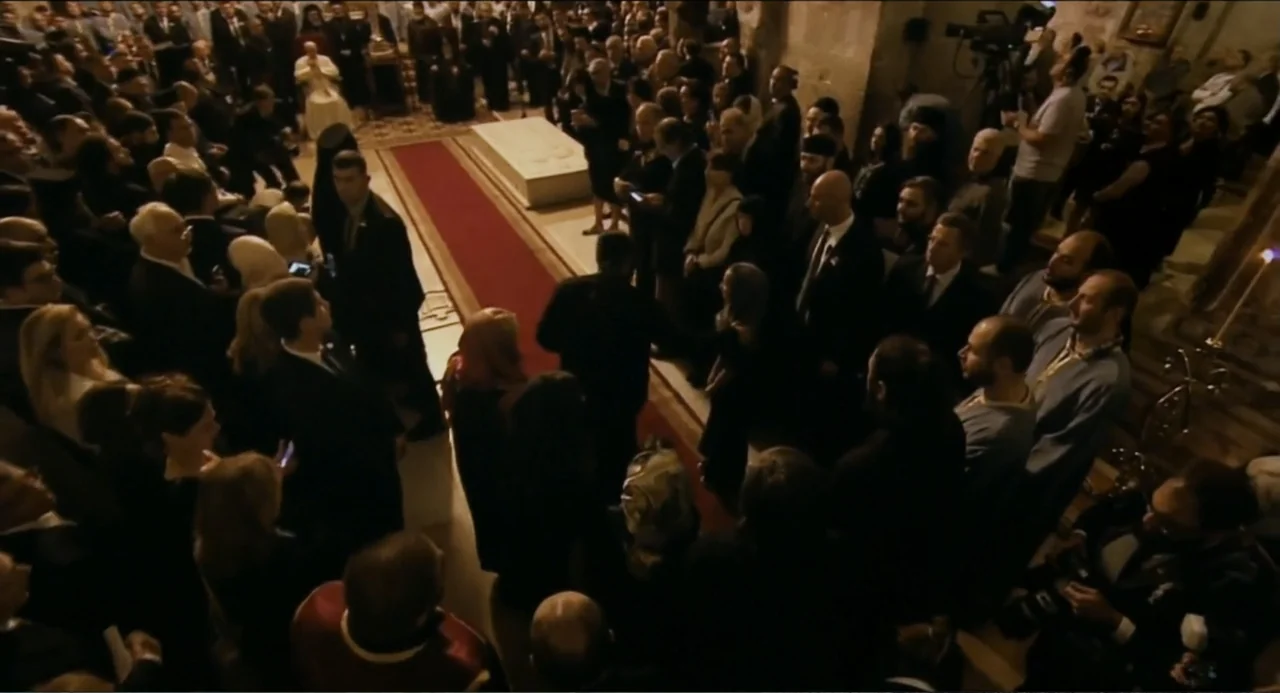 Pope Francis: A Man of His Word (2018) movie still: wide — A crowded stone cathedral interior features a long red carpet leading to a sarcophagus.…