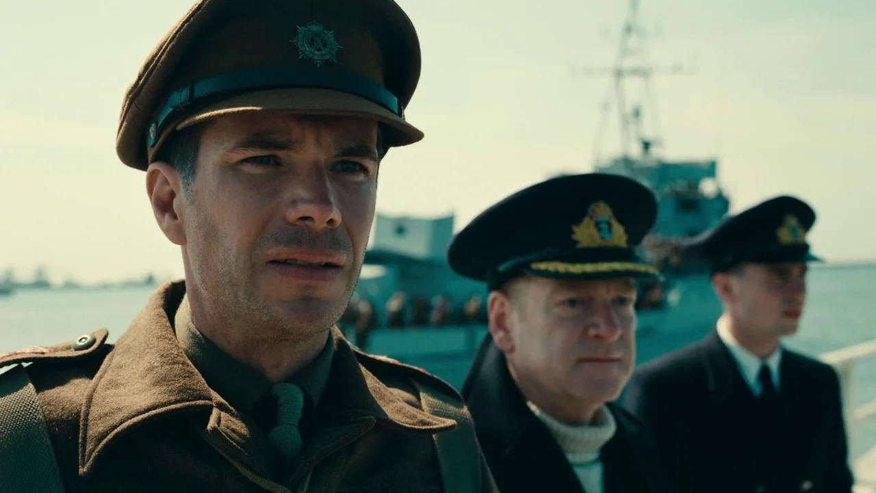 Dunkirk (2017) movie still: medium — A military ship deck with three officers in uniform looking out toward the sea. The men stand in a line on the…