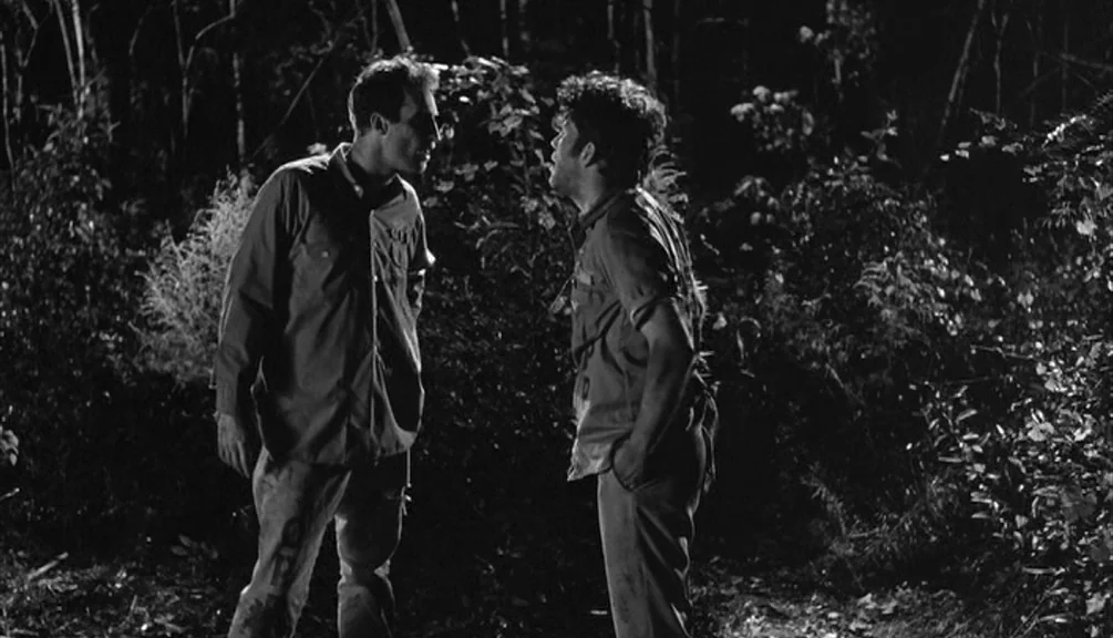 Down By Law (1986) movie still: fullbody — A dense patch of dark woods with thick foliage surrounding two standing figures. The two men face each…
