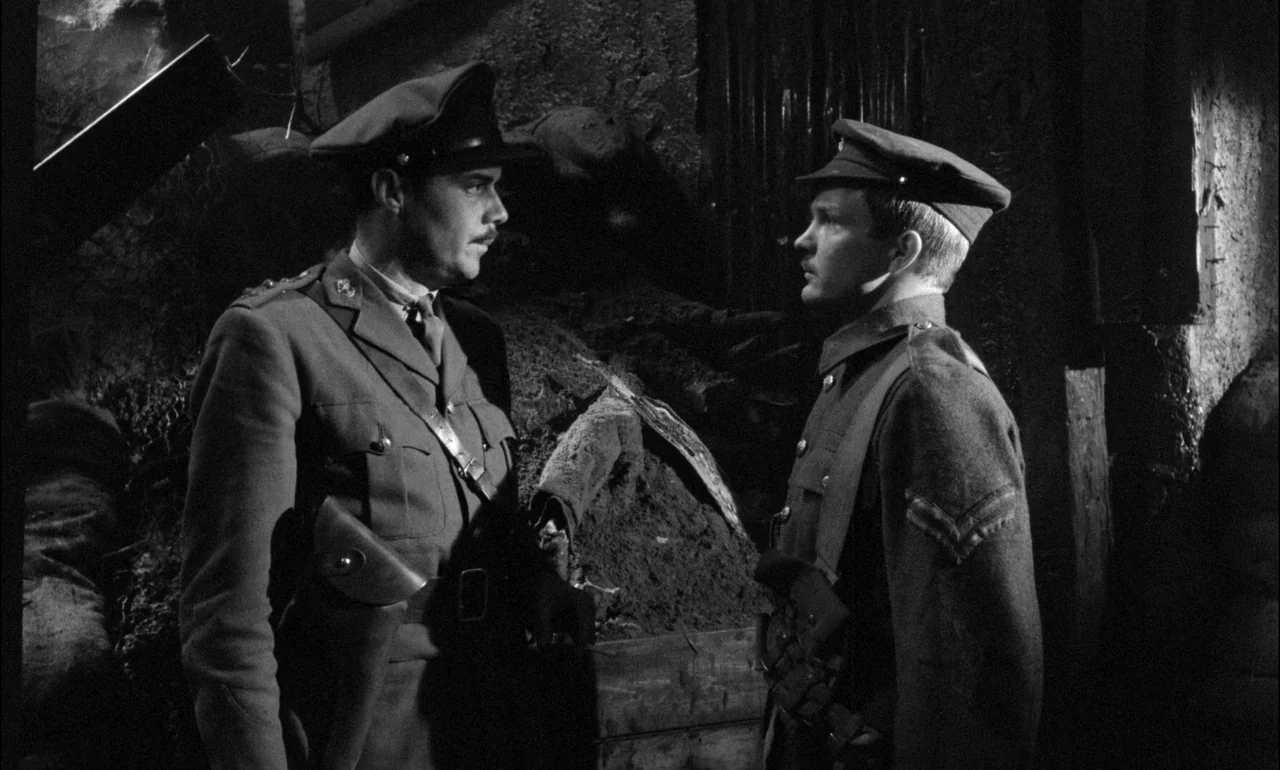 King & Country (1964) movie still: medium — A dimly lit subterranean military bunker features rough stone walls and piles of earth. Two soldiers in…