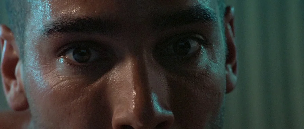 The Big Blue (1988) movie still: closeup — A close-up view shows a man's face illuminated by a cold light source. The man looks directly into the…