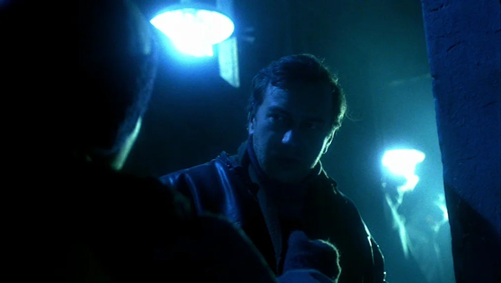 O-Bi, O-Ba: The End of Civilization (1985) movie still: medium — A dark urban alley illuminated by harsh artificial blue light from above. A man…