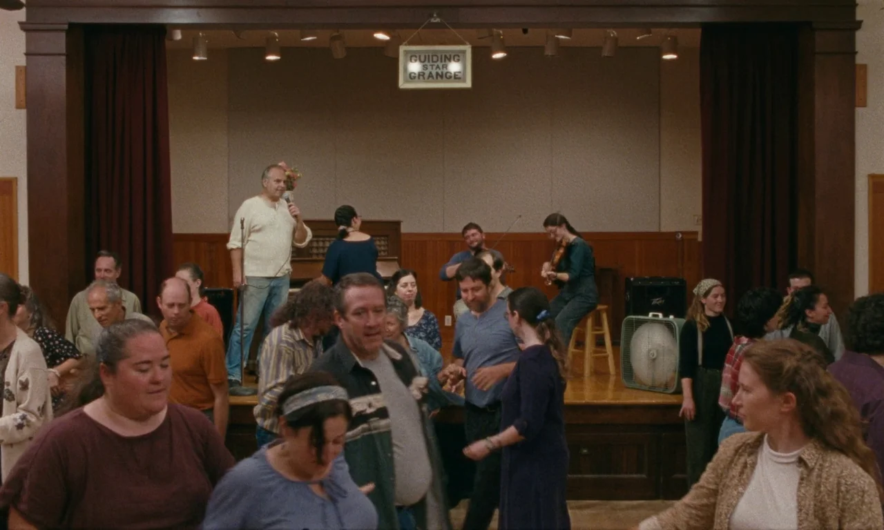 Janet Planet (2023) movie still: wide — A wooden community hall interior features a stage with a band performing for dancers. Various adults in…