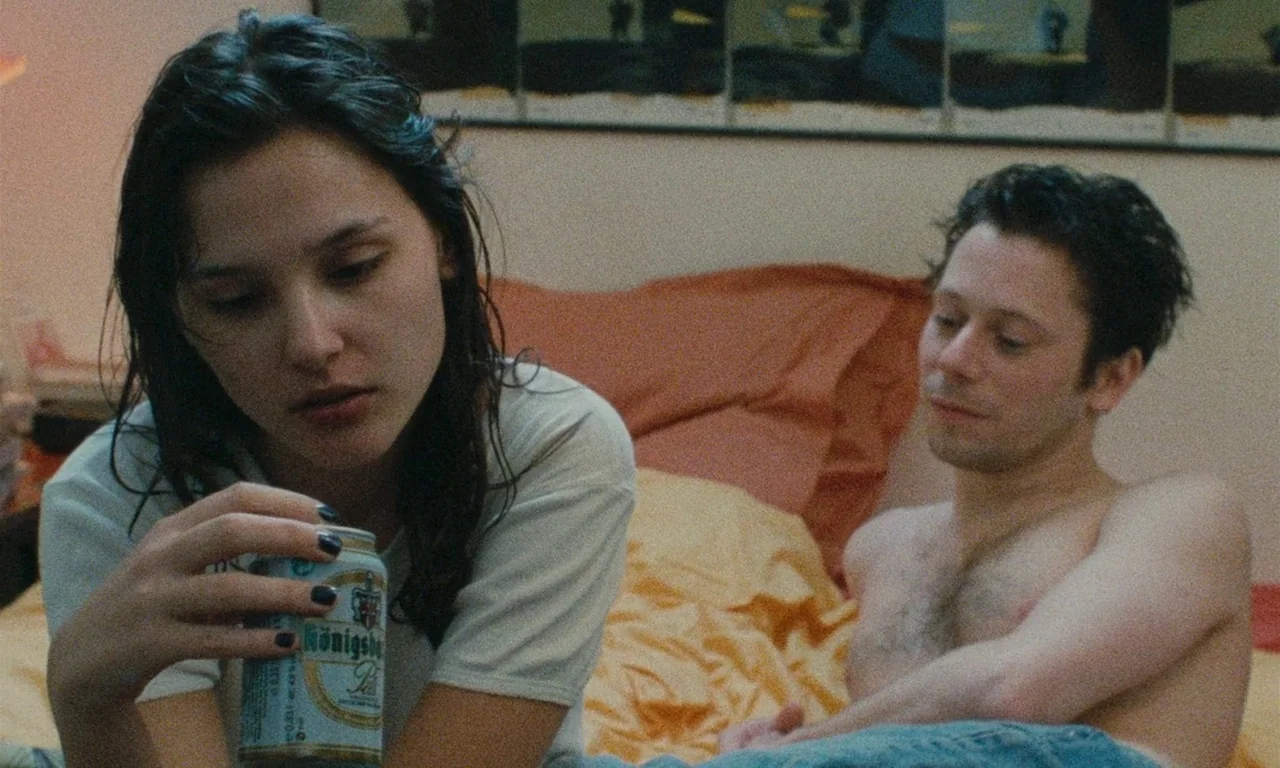 Late August, Early September (1998) movie still: medium — A cluttered bedroom with warm orange bedding and a series of framed art prints. A young…