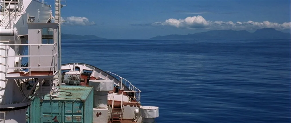 The Intruder (2004) movie still: establishing — A view from the bow of a large ship across the deep blue ocean. Distant landmasses are visible on…