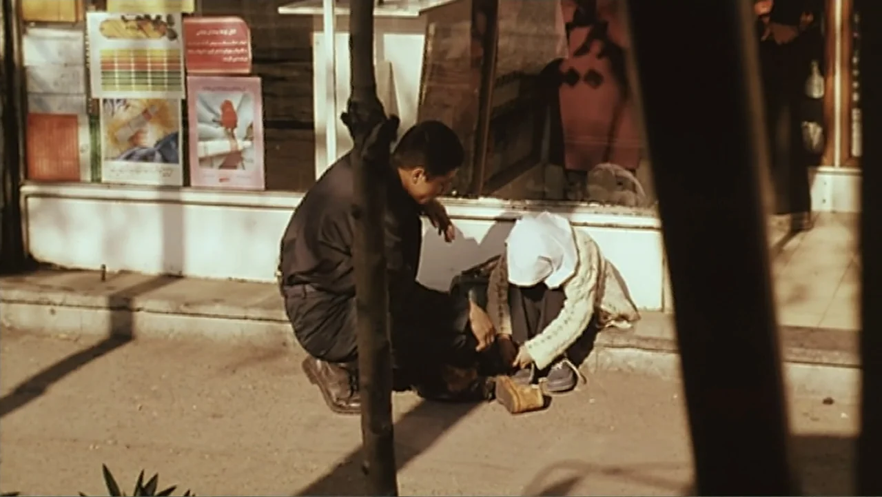 The Mirror (2014) movie still: medium — An urban sidewalk sits in front of a storefront window with paper advertisements. A man kneels on the…