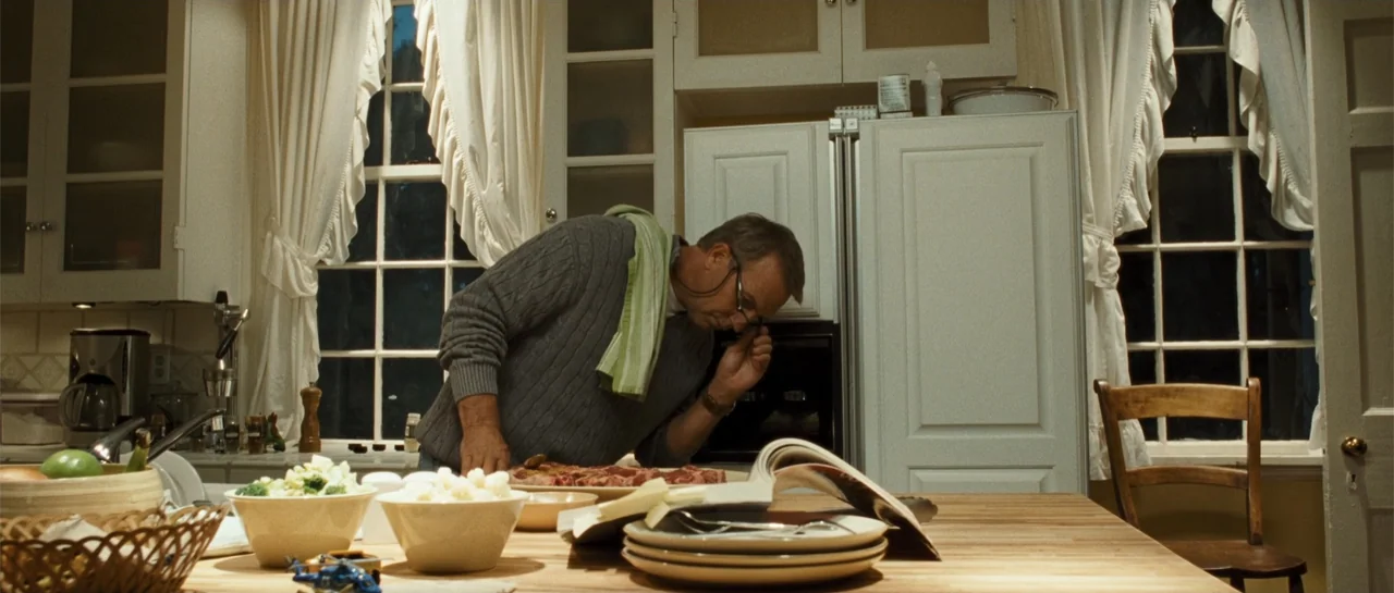The New Daughter (2009) movie still: medium — A well-lit residential kitchen features white cabinetry and a wooden island surface. A middle-aged man…