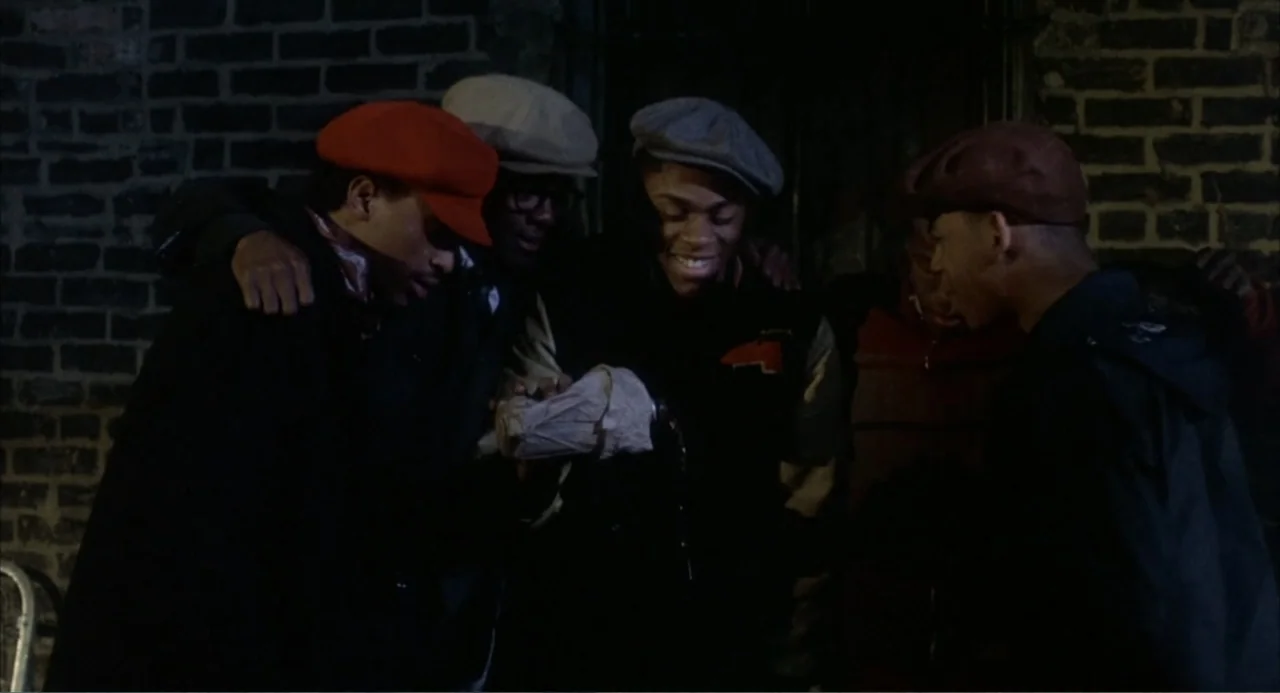 Cooley High (1975) movie still: medium — A dark brick wall provides the backdrop for a small group of men at night. They stand close together while…