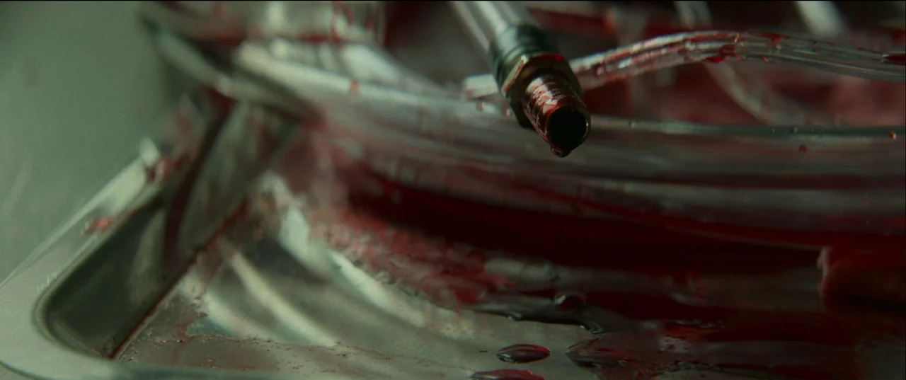 Birth/Rebirth (2023) movie still: closeup — A stainless steel tray holds clear plastic medical tubing coated in fresh, bright blood. A single drop…