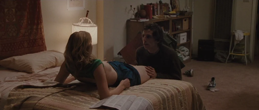 Greenberg (2010) movie still: medium — A cluttered apartment room features a bed covered in a patterned quilt. A man and a woman are positioned…