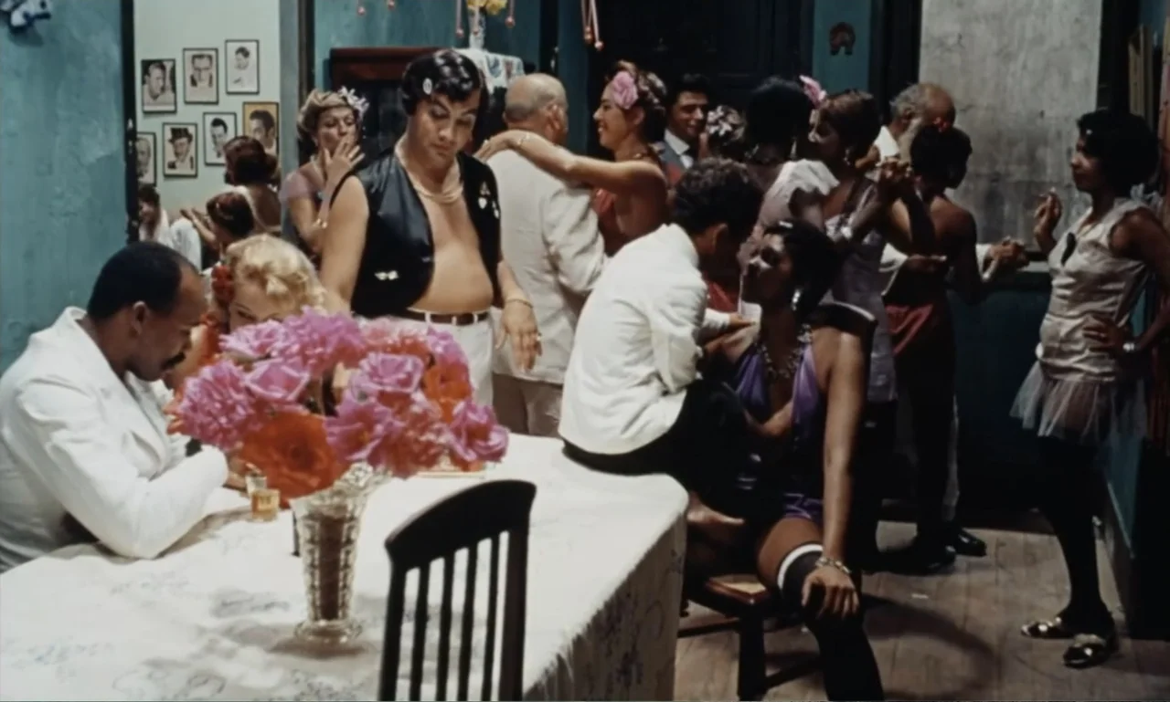 Dona Flor and Her Two Husbands (1976) movie still: medium — A crowded 1970s social space features blue-painted walls covered with numerous framed…