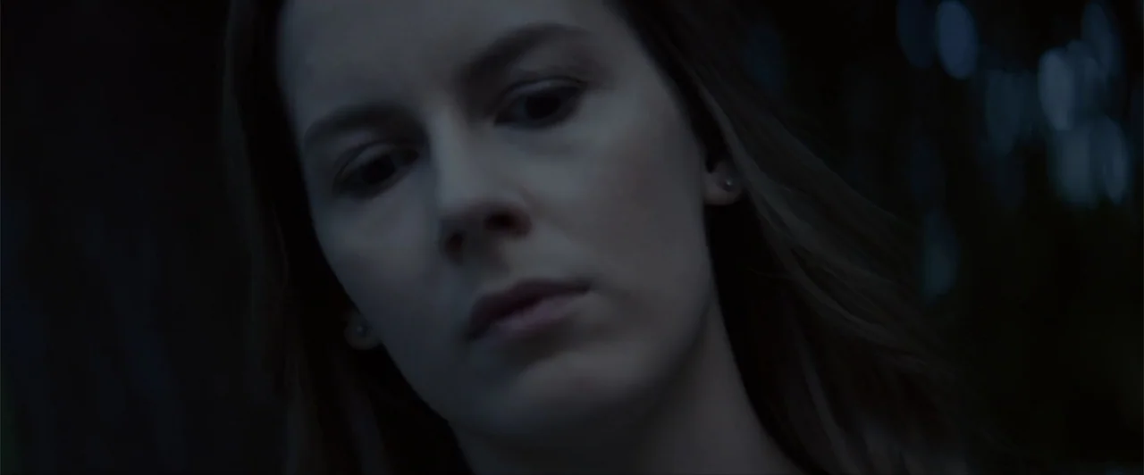 La herencia (2010) movie still: closeup — A dark indoor space contains a person illuminated by subtle blue light. The woman looks downward while the…