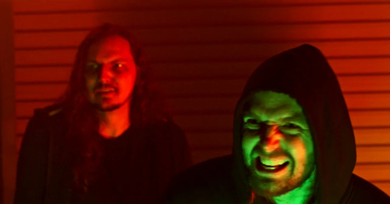 T Blockers (2023) movie still: medium — A dimly lit indoor corridor with horizontal paneled walls reflecting red and green light. A man in a hoodie…