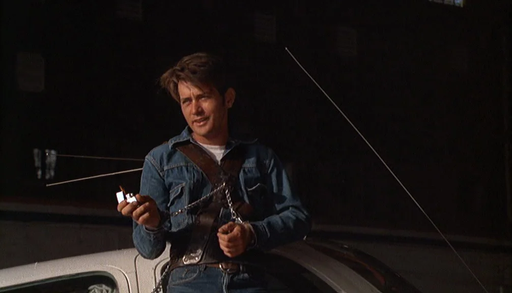 Badlands (1973) movie still: medium — A man stands outdoors at night next to the white roof of a car. He leans on the vehicle while looking toward…