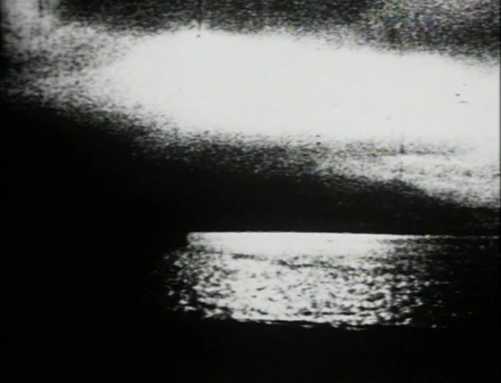 Begotten (1989) movie still: establishing — A dark, textured surface of water reflects a bright source of light from above. The surrounding…