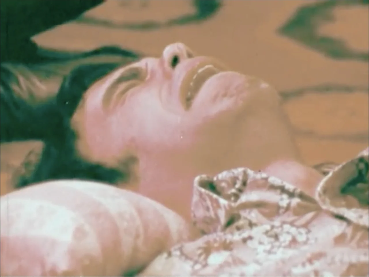 One to One: John & Yoko (2025) movie still: closeup — A close-up of a person lying on a patterned surface inside a room. The individual has their…