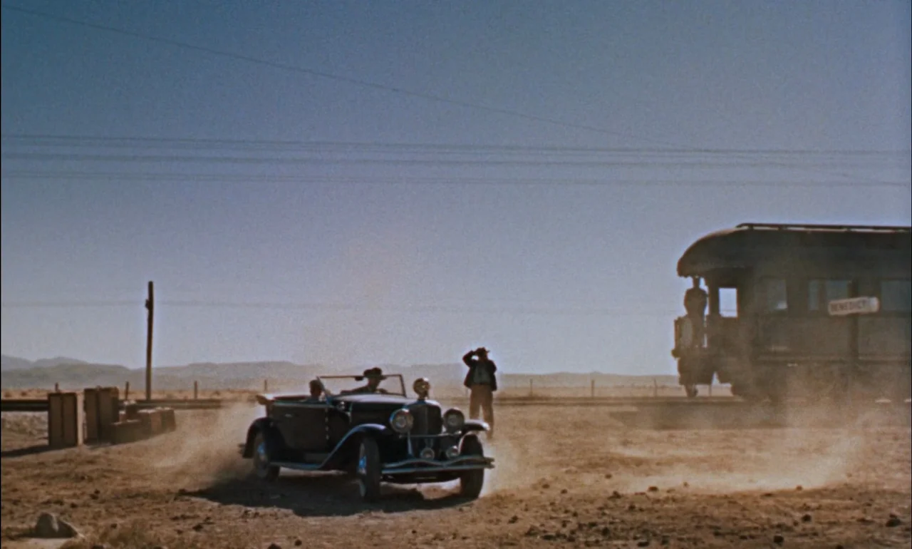 Giant (1956) movie still: wide — A desolate desert landscape features a dusty track next to a stationary railcar. A vintage convertible vehicle…