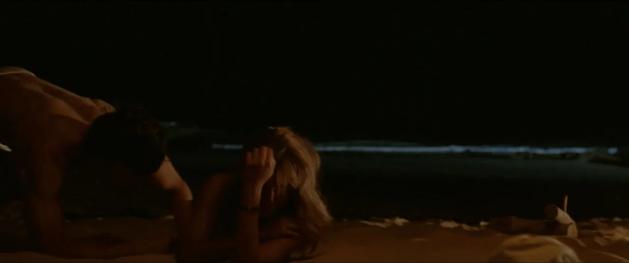 Hear Me: Our Summer (2024) movie still: medium — A dark, sandy shoreline at night with the ocean visible in the background. A man and a woman lie…