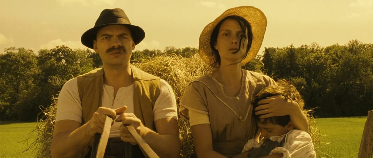 A Very Long Engagement (2004) movie still: medium — A rural agricultural scene featuring a haystack on a wooden cart. A family of three travels…