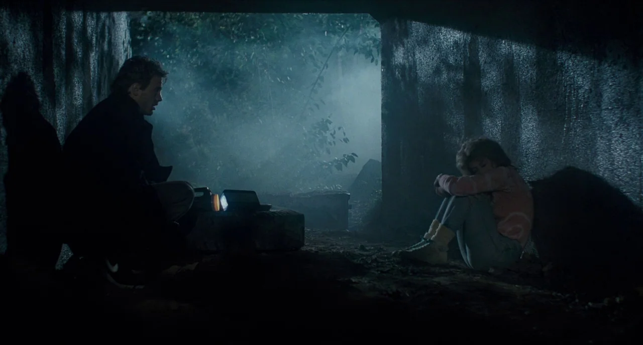 The Terminator (1984) movie still: wide — A dark concrete drainage culvert is filled with thick fog and low-hanging vegetation outside. A man and a…