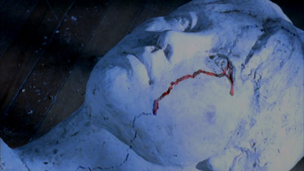 Whispering Corridors (1998) movie still: closeup — A plaster head sculpture rests on dark, scratched wooden planks. A single jagged crack runs…