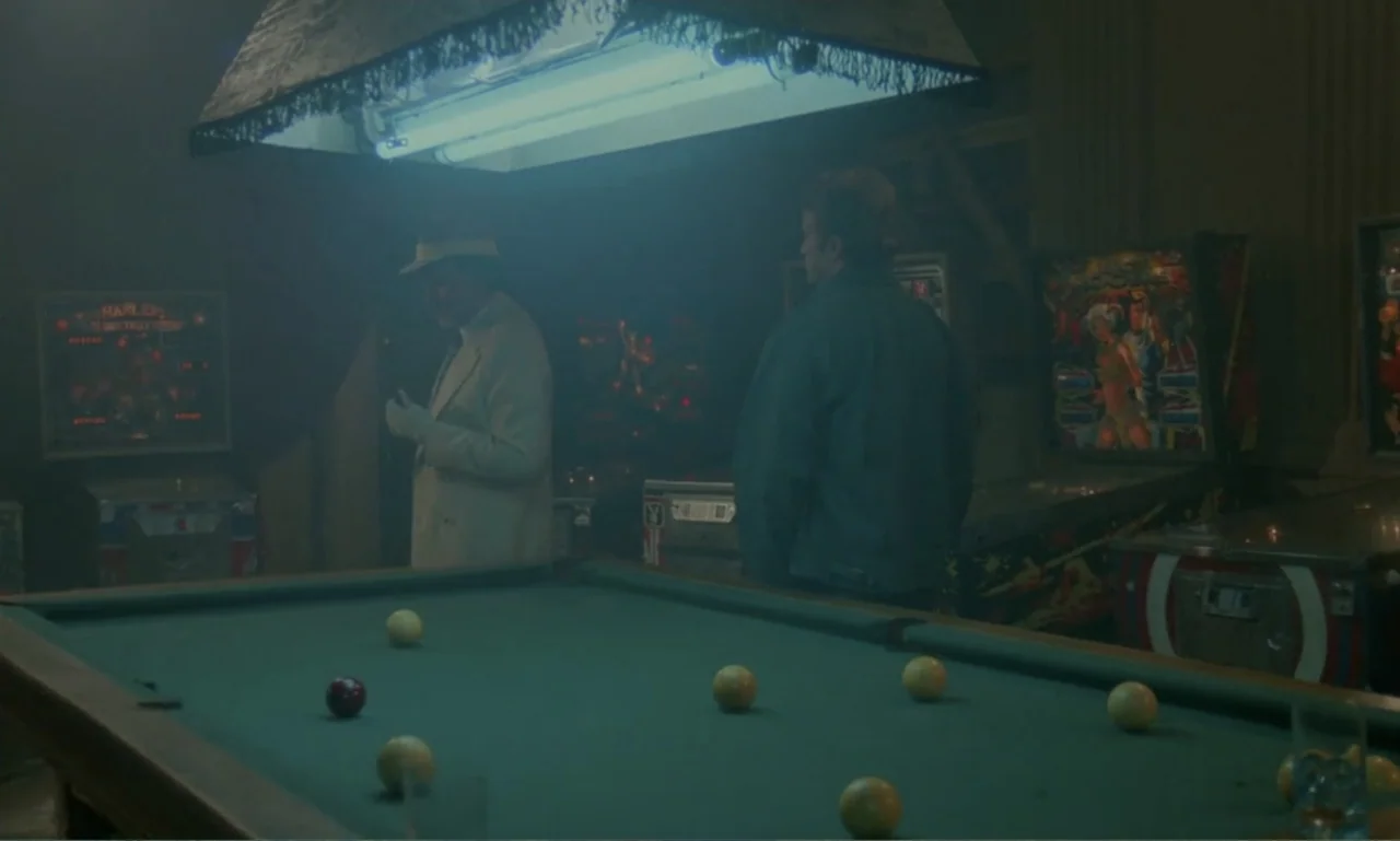 Ga-ga: Glory to the Heroes (1986) movie still: medium — A smoky room with vintage pinball machines and a pool table under fluorescent lighting. Two…