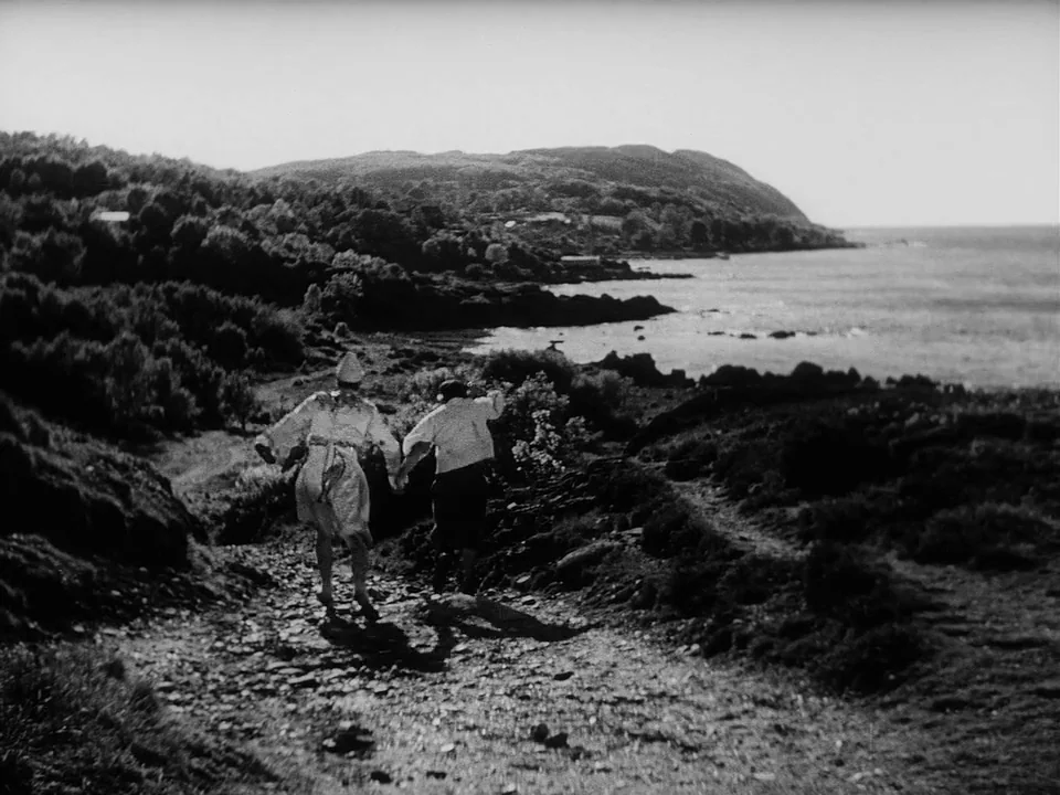 Sawdust and Tinsel (1953) movie still: wide — A rugged coastal trail overlooks a calm sea bordered by dense hilly vegetation. Two people run…