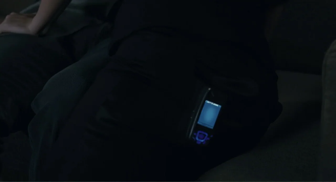 Because I Said So (2007) movie still: closeup — A dark, out-of-focus fabric surface supports a small electronic device. An illuminated mobile phone…