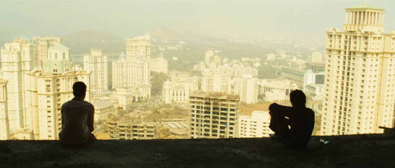 Slumdog Millionaire (2008) movie still: wide — A high-rise concrete rooftop overlooks a sprawling city with numerous tall, modern apartment…