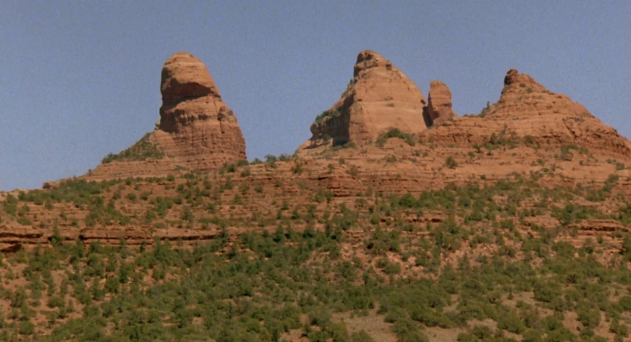 The Karate Kid (1984) movie still: wide — Red sandstone rock formations rise above a scrub-covered desert slope under a clear sky. The arid…