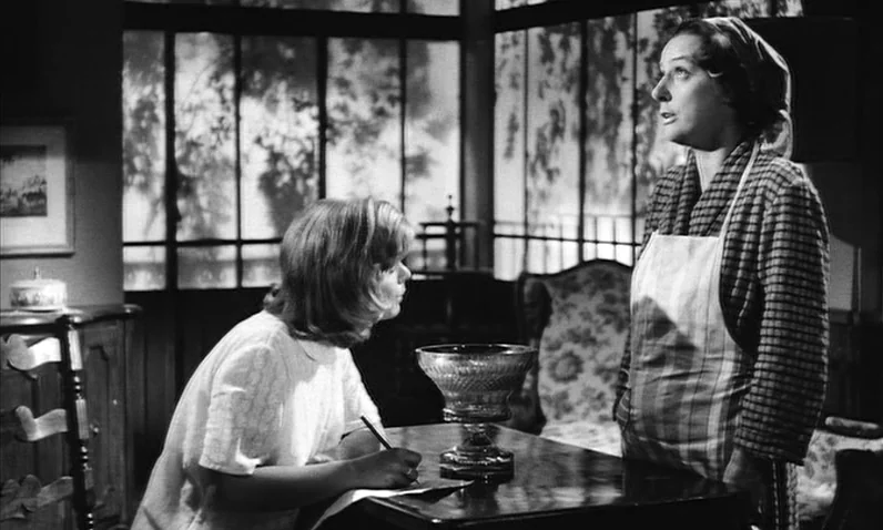 The Girl Who Knew Too Much (1963) movie still: medium — A furnished dining area features a large window with multiple panes overlooking exterior…