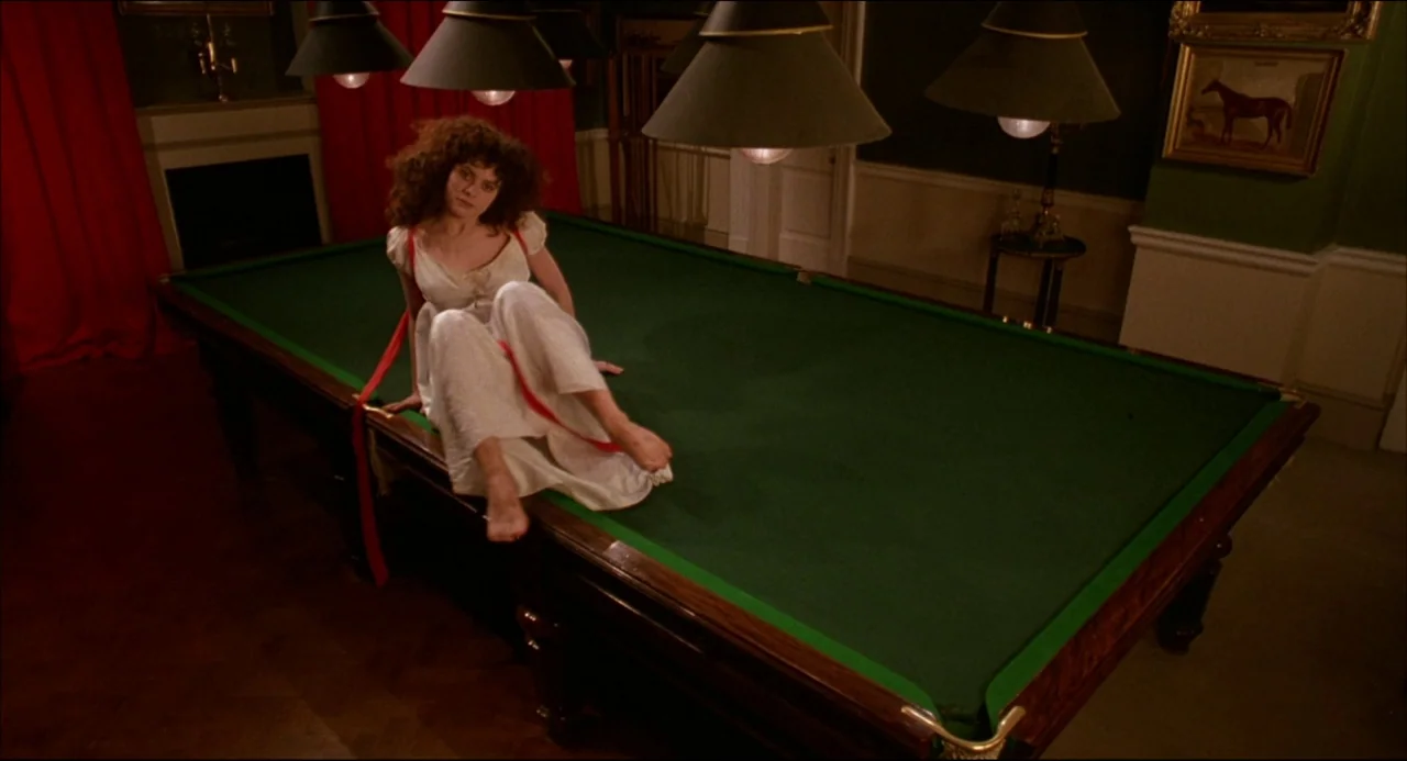 Gothic (1986) movie still: fullbody — A dark, wood-paneled room features a large green felt billiard table under pendant lamps. A woman in a white…