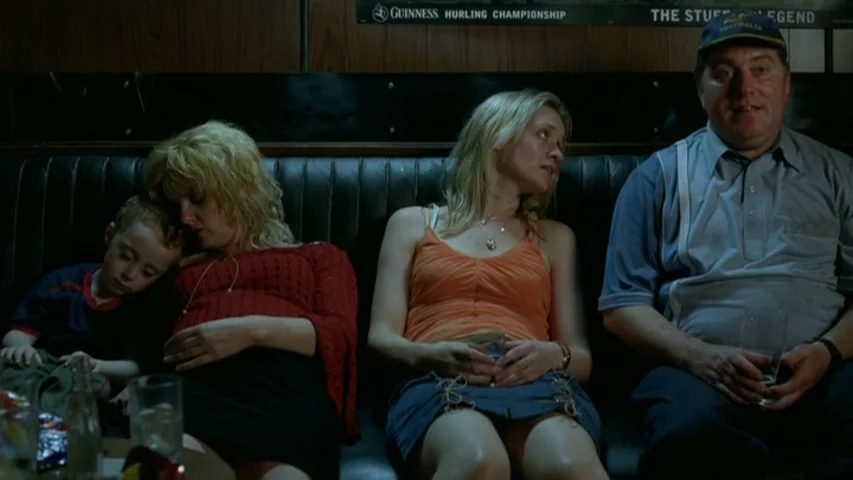 Garage (2007) movie still: medium — A dimly lit pub booth features wood paneled walls with a faded advertisement poster. Four people sit side by…