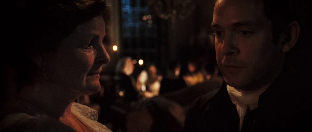 Pride & Prejudice (2005) movie still: medium — A dimly lit room features a woman and a man in close proximity. Other blurred figures dine in the…