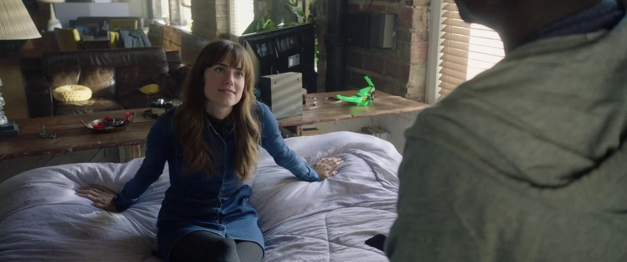 Get Out (2017) movie still: medium — A furnished loft-style bedroom features exposed brick walls and a large wooden desk. A young woman with brown…