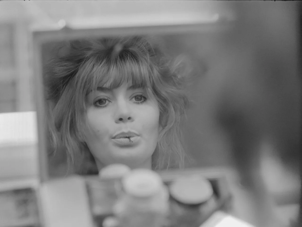 The Baby Carriage (1963) movie still: closeup — A woman stares into a framed mirror in a brightly lit dressing room space. She holds a small…