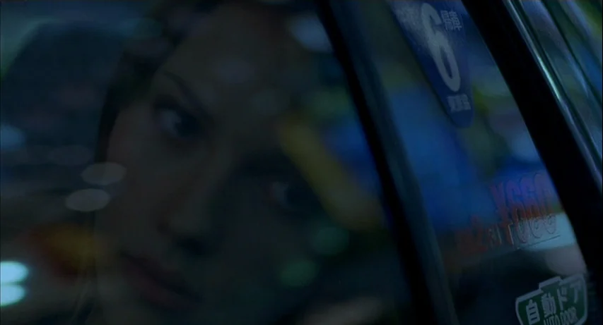 Lost In Translation (2003) movie still: closeup — The interior of a moving vehicle at night seen through the passenger window glass. A young woman's…