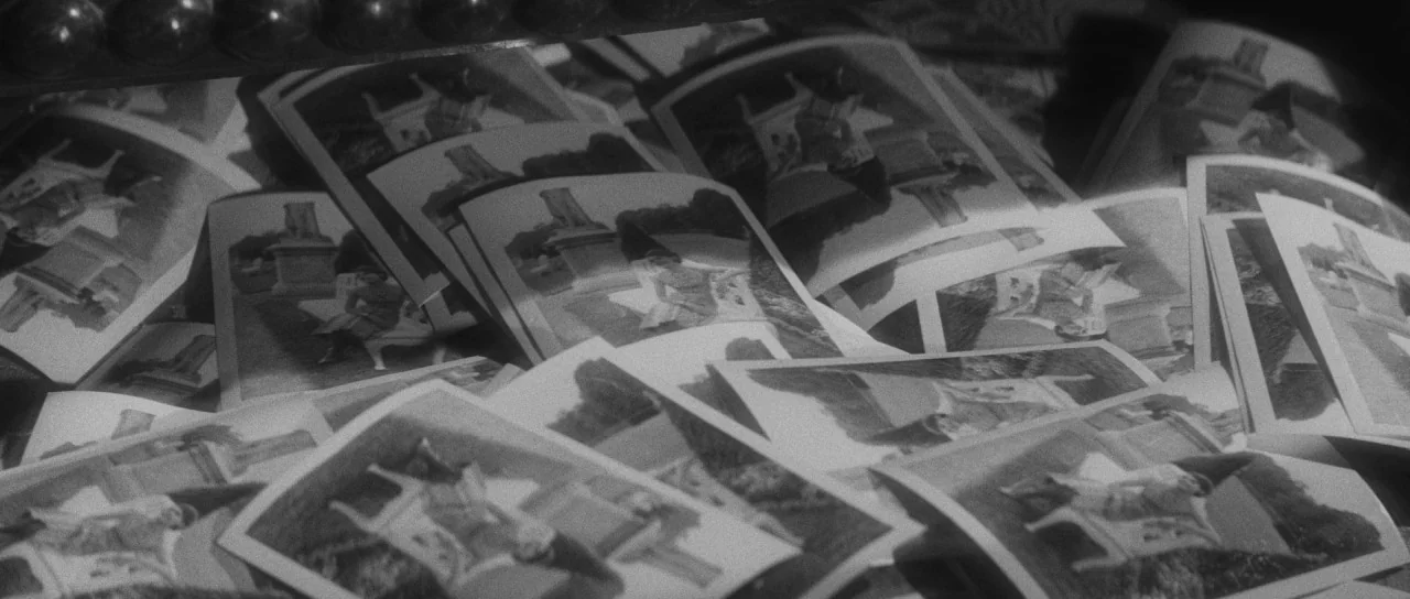 Last Year at Marienbad (1961) movie still: closeup — A pile of black and white photographs are scattered across a dark surface. Each print depicts a…