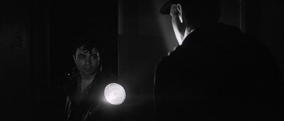 In Cold Blood (1967) movie still: medium — A dimly lit, dark space obscures most architectural detail in the background. Two men stand in close…