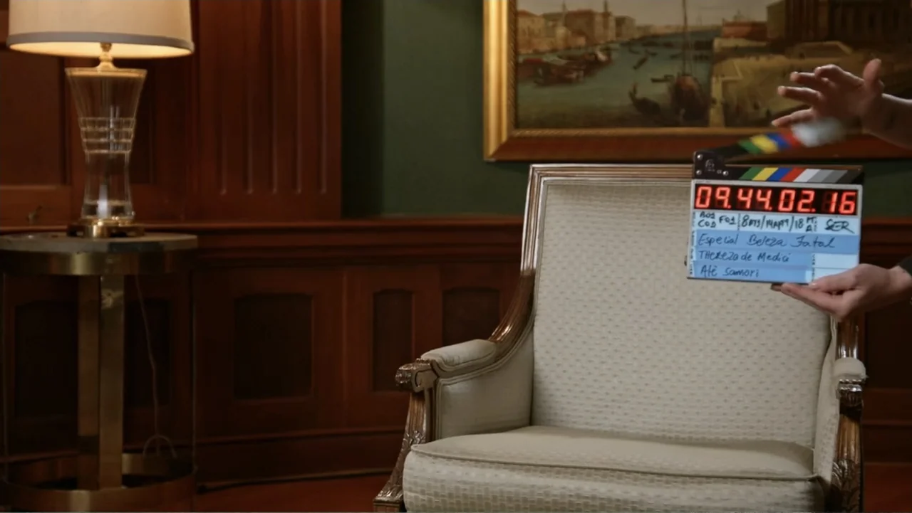 Making of: Scars of Beauty (2025) movie still: medium — A wood-paneled room features a beige armchair and a classic landscape painting on the wall.…