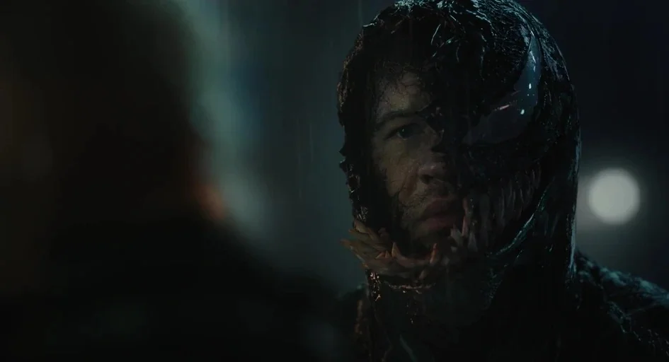Venom Let There Be Carnage (2021) movie still: closeup — A dark, rain-slicked urban setting at night provides a dim backdrop. A man's face is…