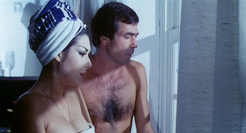 5 Dolls for an August Moon (1970) movie still: medium — A light-filled interior space with a window and white curtains visible in the background. A…