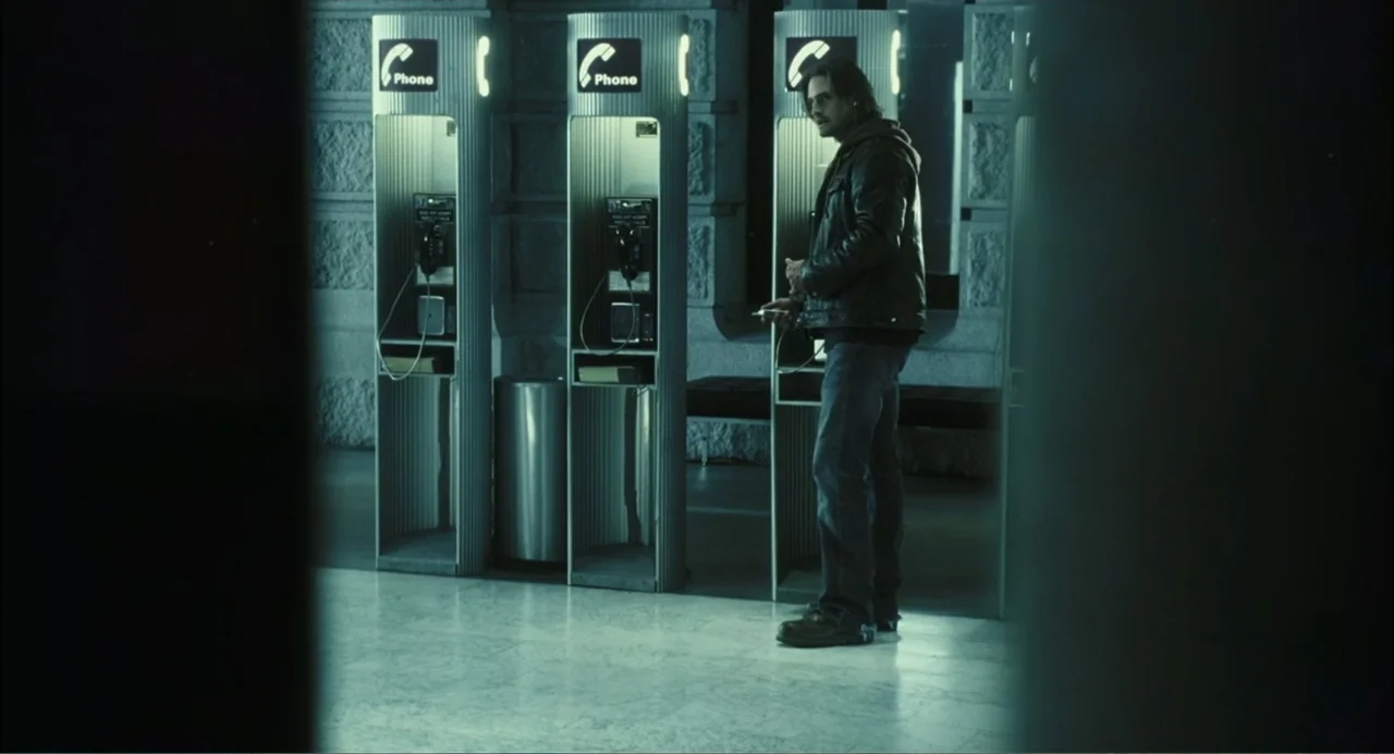 El hijo del diablo (1966) movie still: fullbody — A quiet lobby contains a series of metal phone booths against a stone wall. A man stands in front…