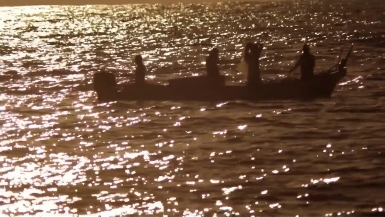 El sueño (2020) movie still: wide — A small wooden boat floats on the surface of the ocean at golden hour. Four people are sitting as silhouettes in…