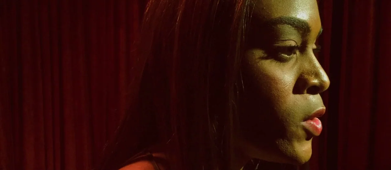 Tangerine (2015) movie still: closeup — A woman stands in front of heavy dark red curtains in an interior space. The subject is captured in a tight…