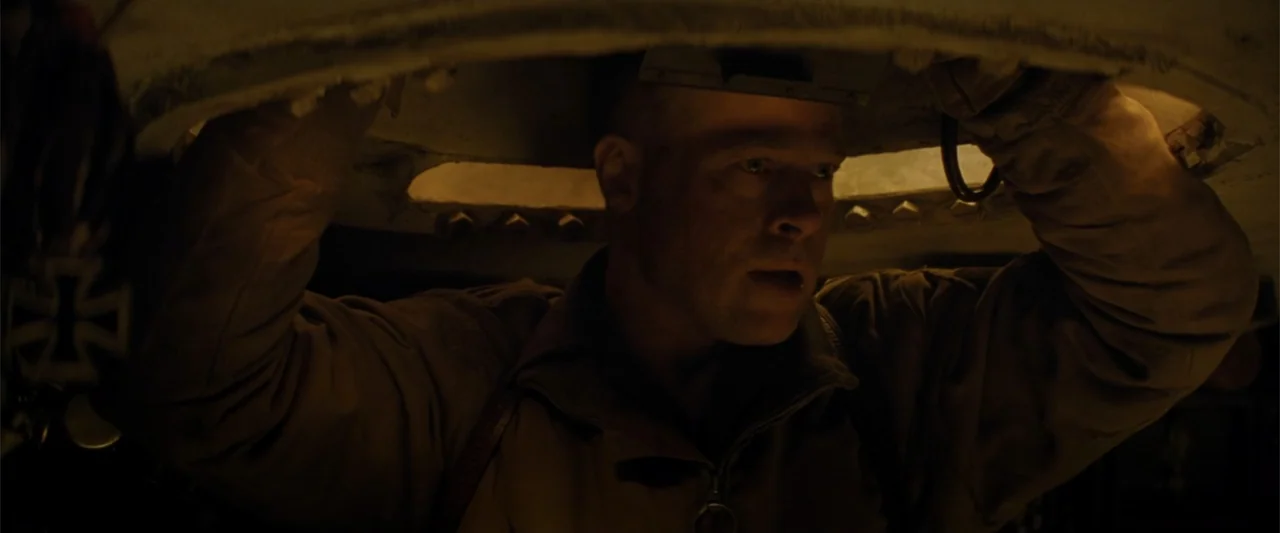 Fury (2014) movie still: closeup — The interior of a metallic armored vehicle is dimly lit from the overhead hatch. A man gazes forward through the…