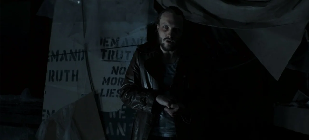 I Still See You (2018) movie still: medium — A dimly lit interior room featuring walls plastered with hand-painted protest signs and plastic…