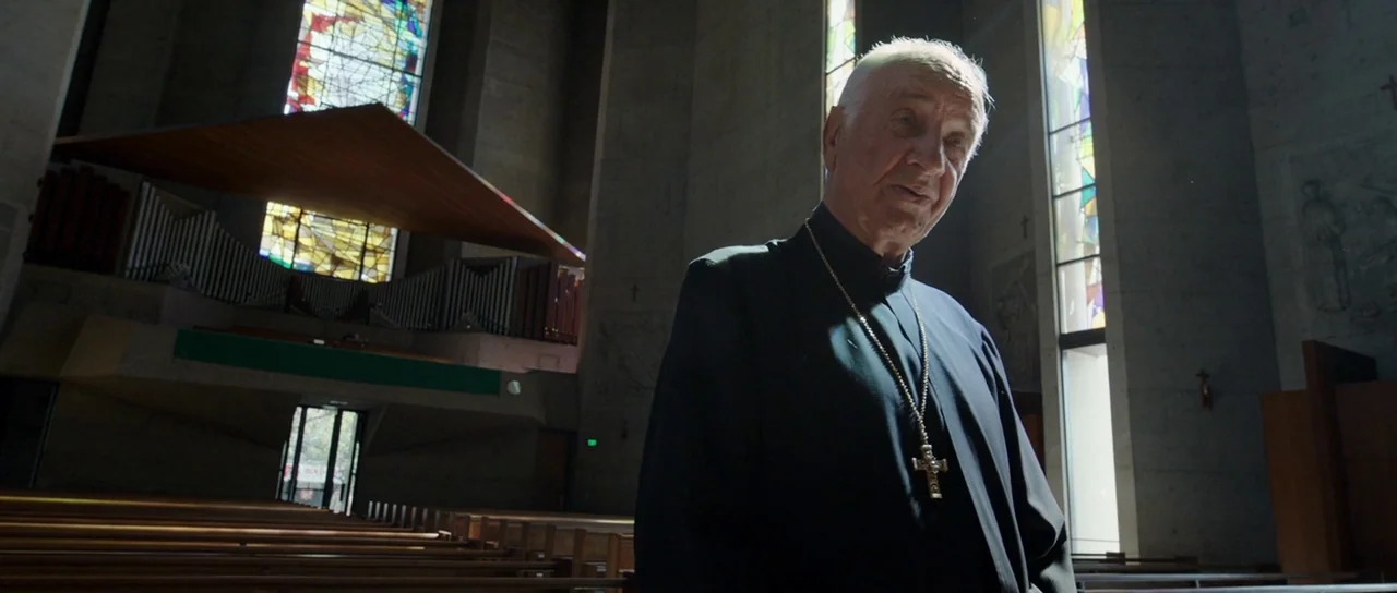 Knight of Cups (2015) movie still: medium — A modern church interior features high concrete walls and geometric stained glass panels. An elderly…