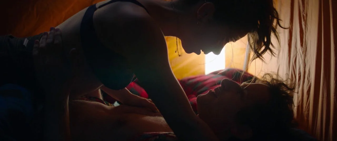 Palm Springs (2020) movie still: medium — Inside a fabric tent with orange walls and a red plaid sleeping bag interior. A woman looms over a man…
